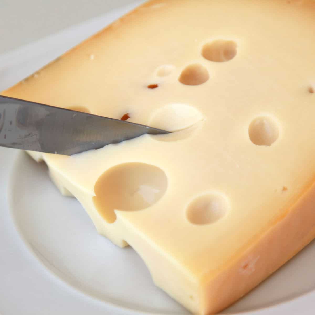 Quadratisches Bild von Schweizer Käse, der geschnitten wird.