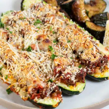 Wide image of zucchini boats with ground beef on white plate.
