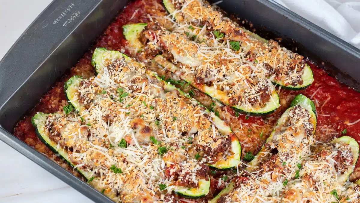 Wide image of zucchini boats with ground beef in baking pan.