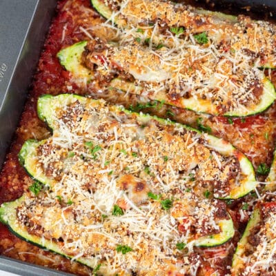 Square image of zucchini boats with ground beef in baking pan.