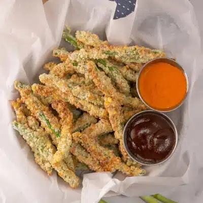 Square image of a basket of air fried green bean fries with dipping sauces.