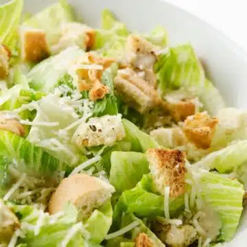 Wide image of Caesar Salad in a white bowl.