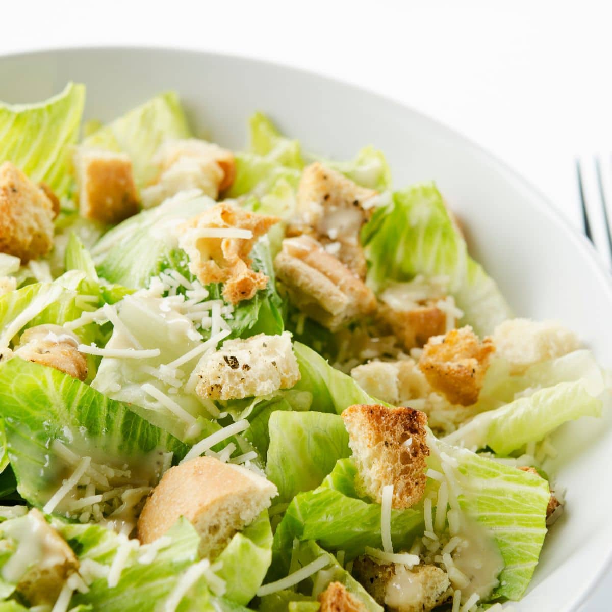 Quadratisches Bild von Caesar Salad in einer weißen Schüssel.