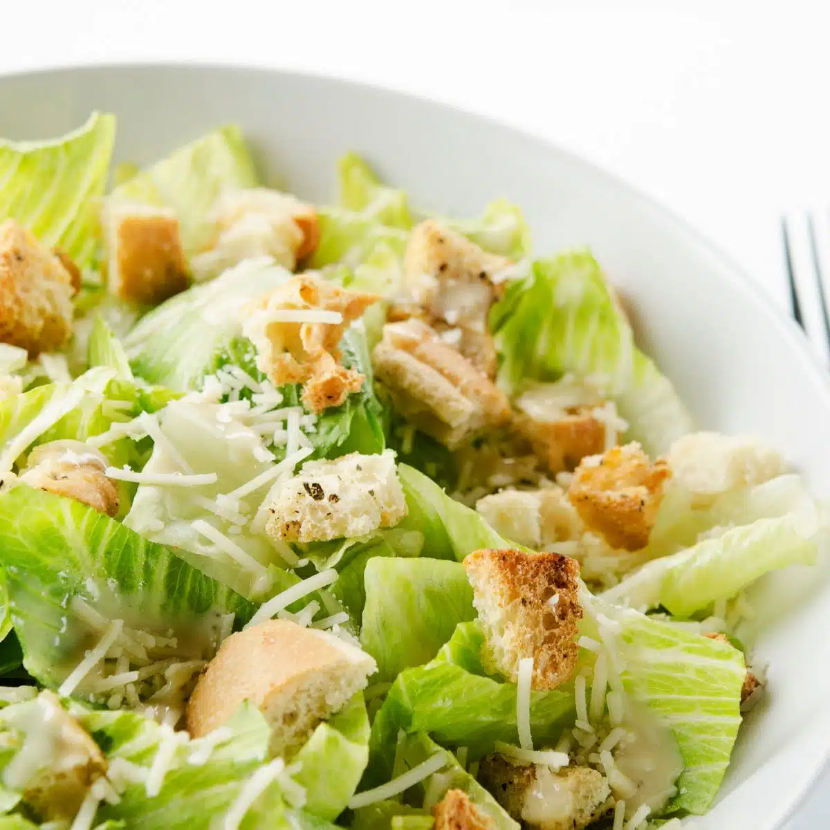 Quadratisches Bild von Caesar Salad in einer weißen Schüssel.