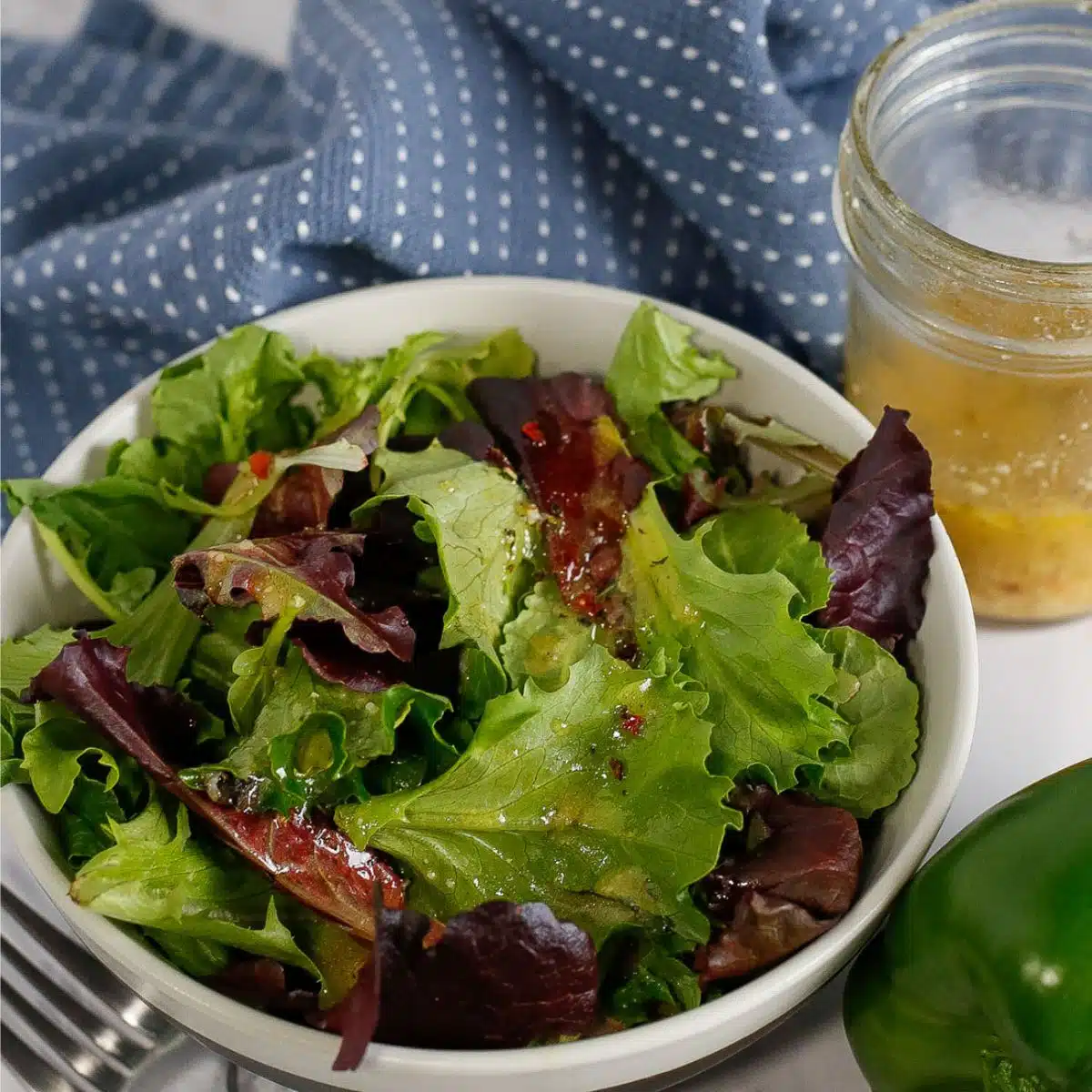 Tasty Italian dressing recipe with homemade dressing in a mason jar and tossed with salad greens in a white bowl.