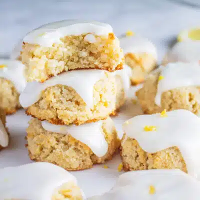Perfect lemon almond cookies with icing and lemon zest on light grey marble surface stacked 3 high with a bite taken from the top cookie.
