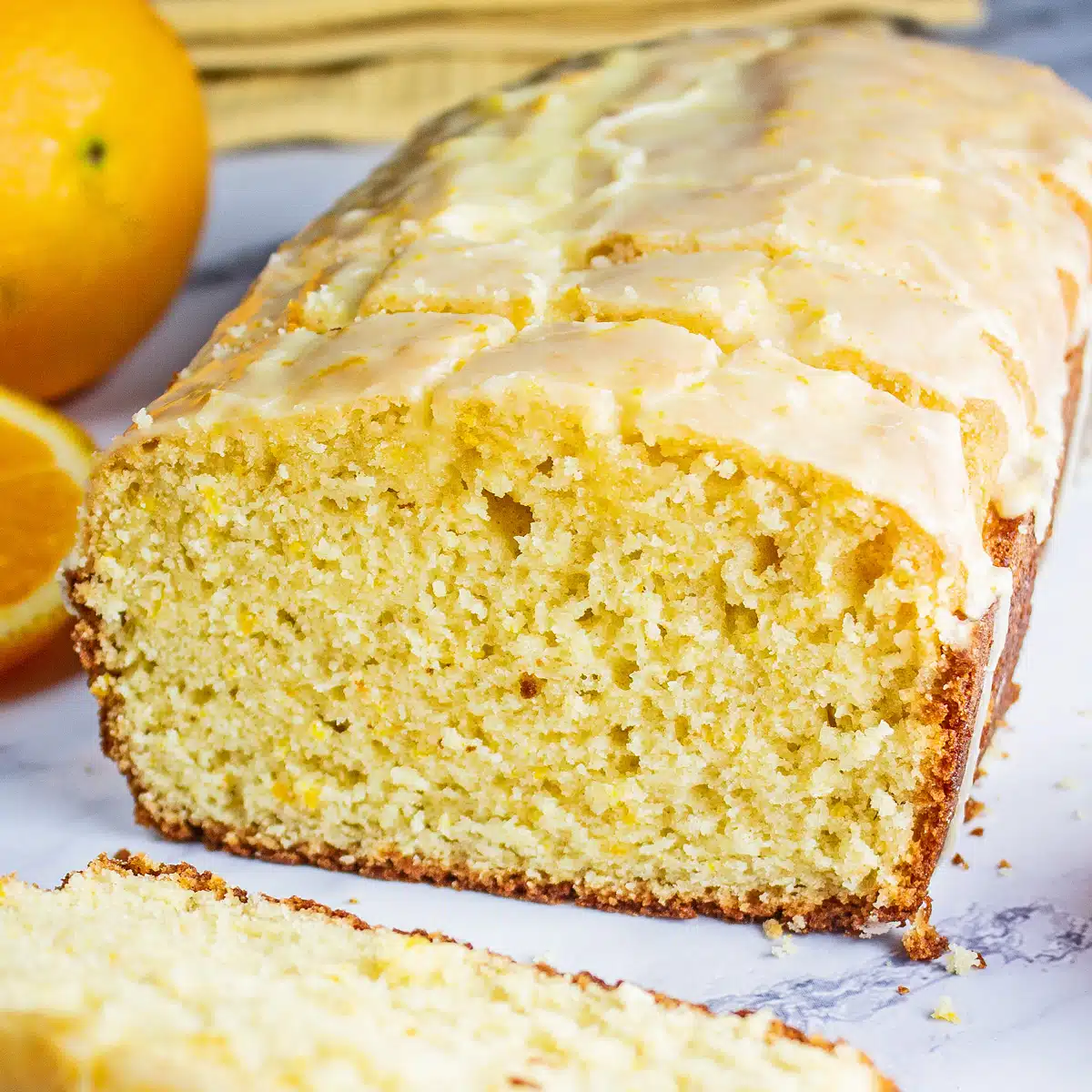 Sliced orange loaf cake with oranges and sliced oranges in the background.