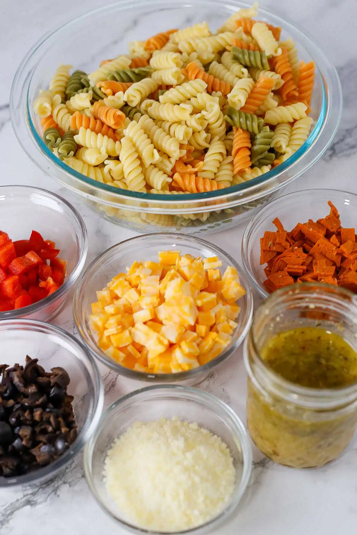 Tall image showing ingredients needed for pasta salad with Italian dressing.