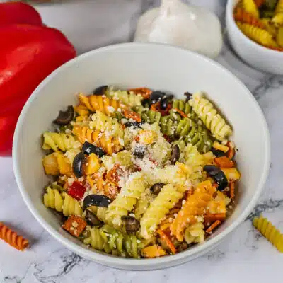 Square image of pasta salad with Italian dressing in a white bowl.