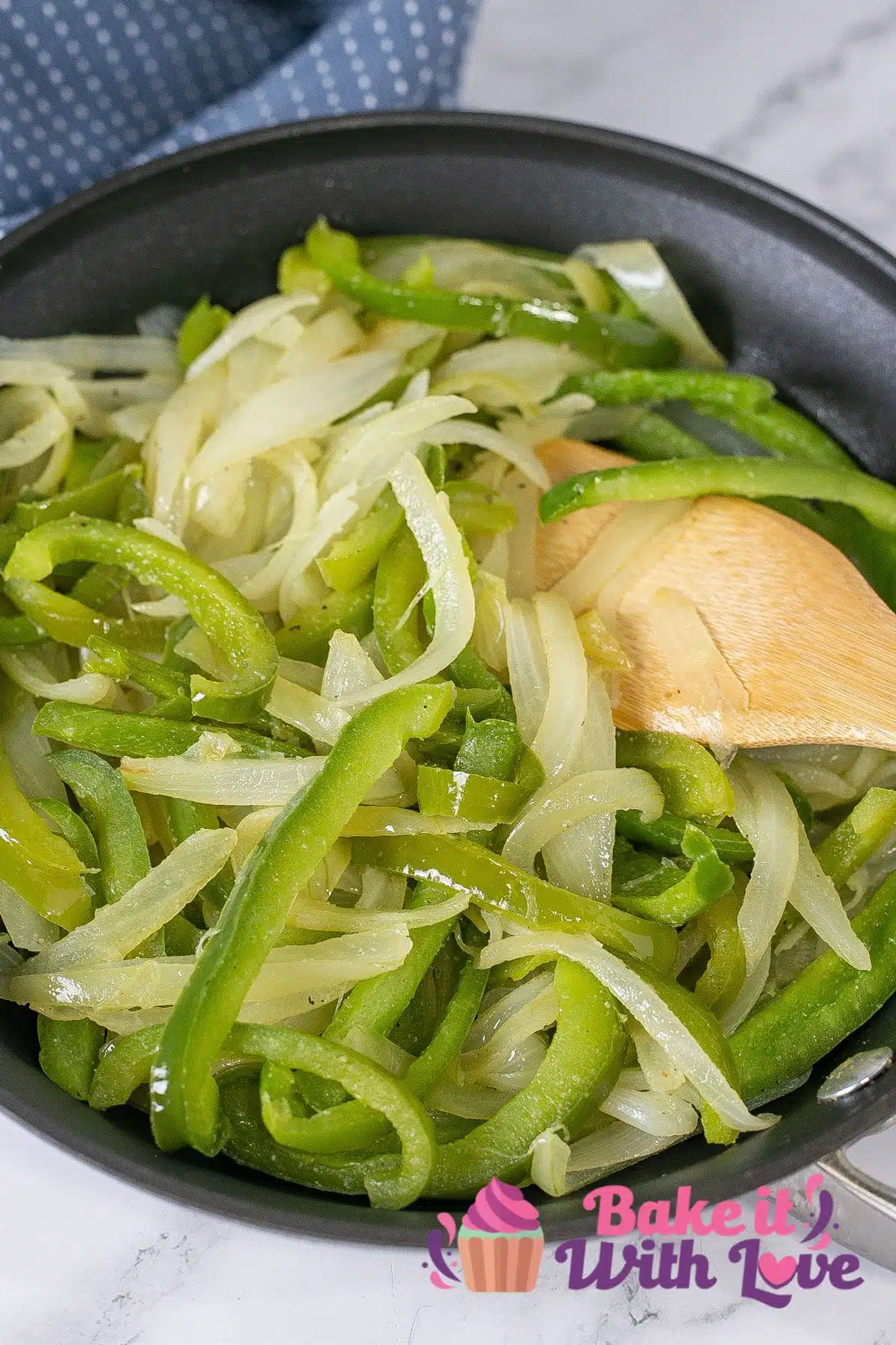 Tall image of sauteed peppers and onions in a skillet with a wooden spoon.