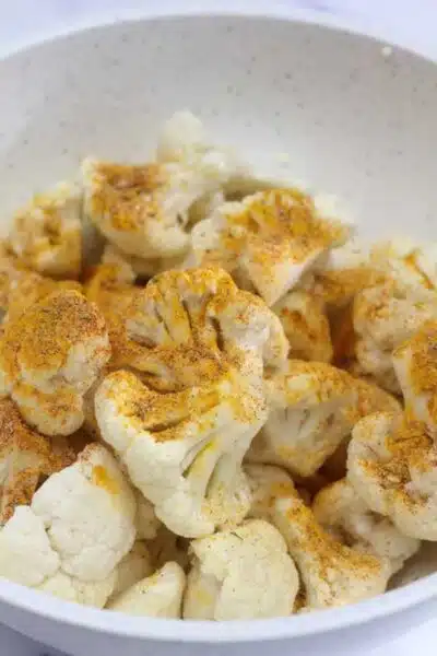 Process image 2 showing cauliflower in a bowl with added seasoning.