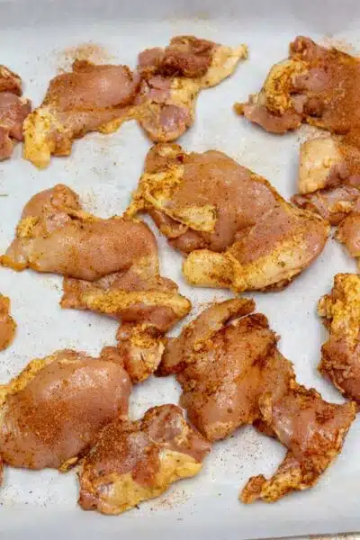 Process image 3 showing seasoned boneless chicken thighs on a baking sheet.