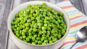 Wide image of a bowl of green peas, cooked from frozen.