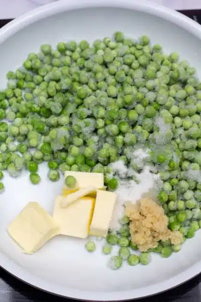 Process image 1 showing garlic, butter, and frozen peas in a skillet.