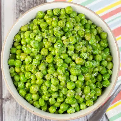 Square image of a bowl of green peas, cooked from frozen.
