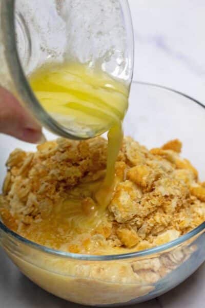 Obrázek procesu 4 znázorňující přidávání rozpuštěného másla do rozdrcených sušenek Ritz.