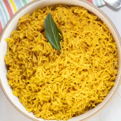 Square image of pilau rice in a white bowl with a bay leaf.