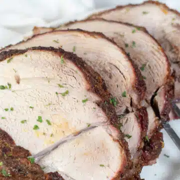 Wide image of sliced pork picnic roast on a white serving platter.