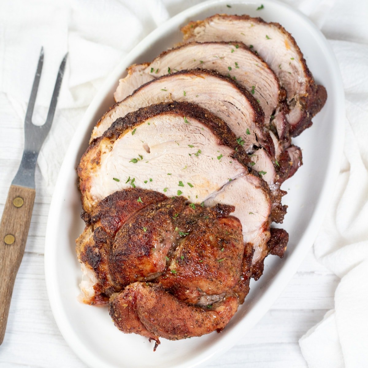 Square image of sliced pork picnic roast on a white serving platter.