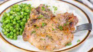 Wide image of ranch pork chops on a plate with peas and rice.