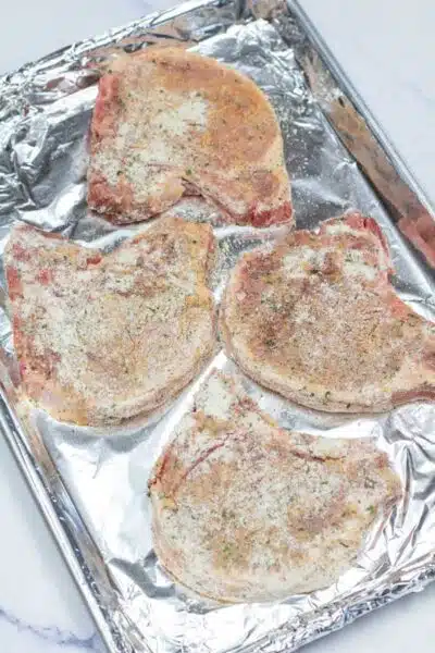 Process image 6 showing pork chops on foil lined baking sheet.