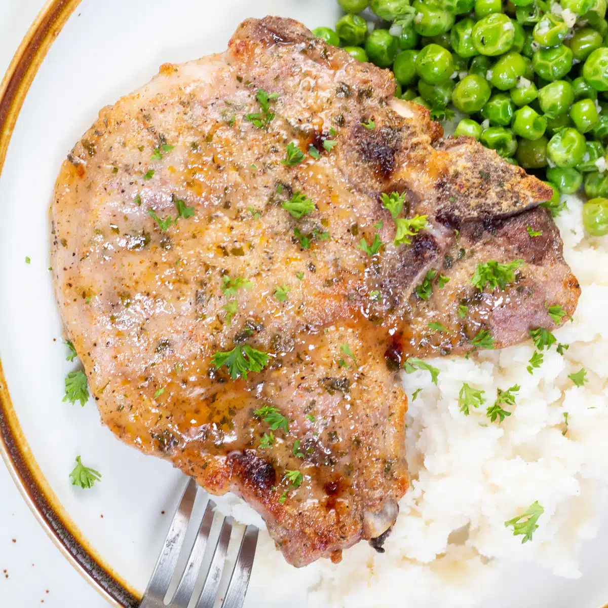Square image of ranch pork chops on a plate with peas and rice.