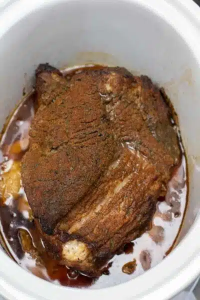 Process image 3 showing brisket in slow cooker with added bbq sauce.