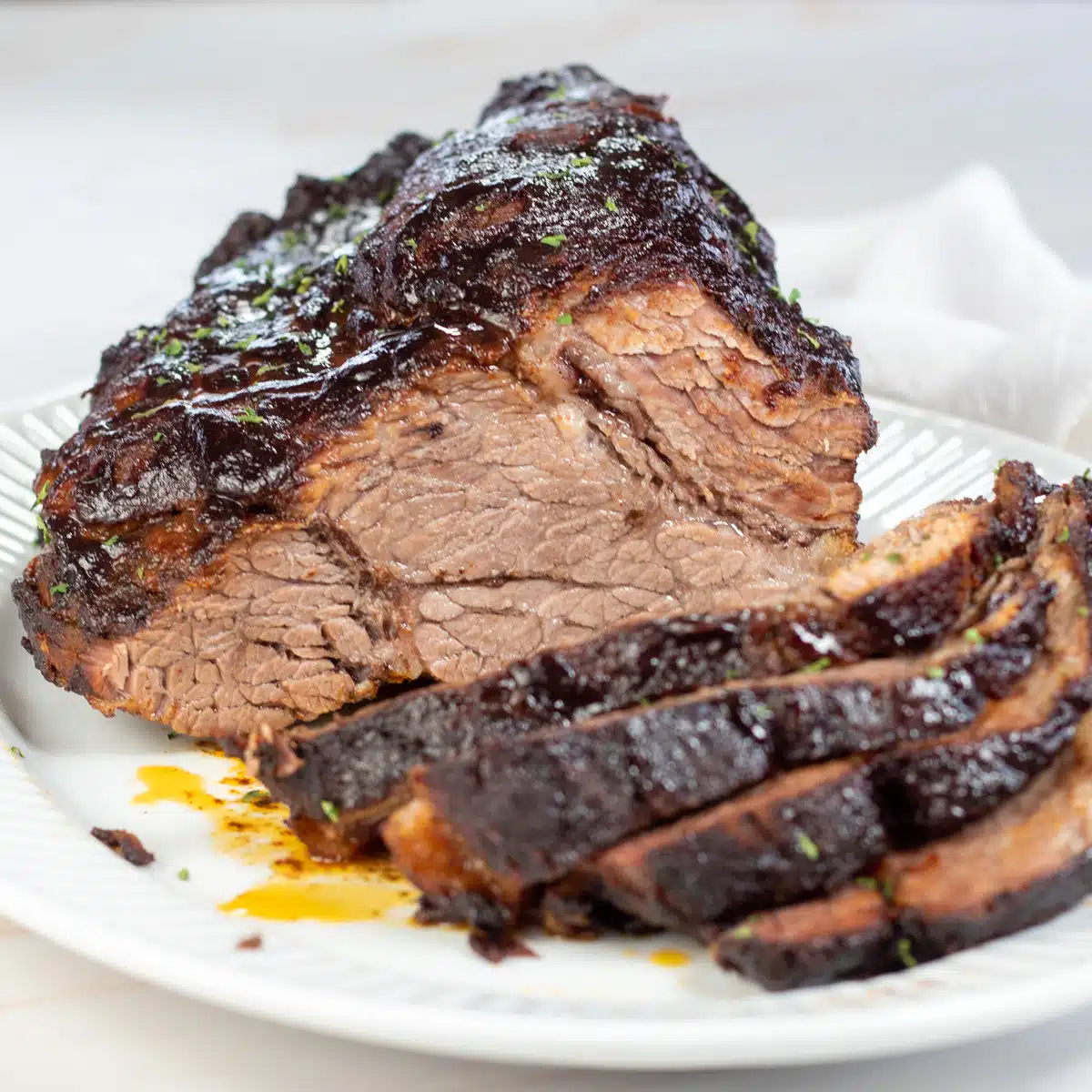 Square image of slow cooker brisket, sliced and on a white serving dish.