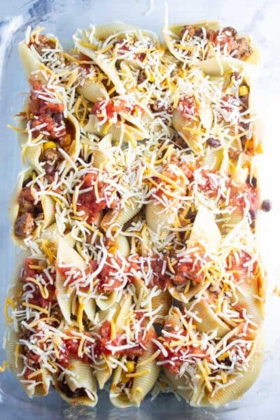 Обработете изображение 8, показващо пълнени макаронени черупки в съд за печене с добавено сирене.