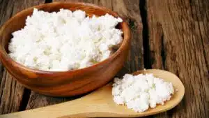Wide image of cottage cheese in a wooden bowl and a wooden spoon.