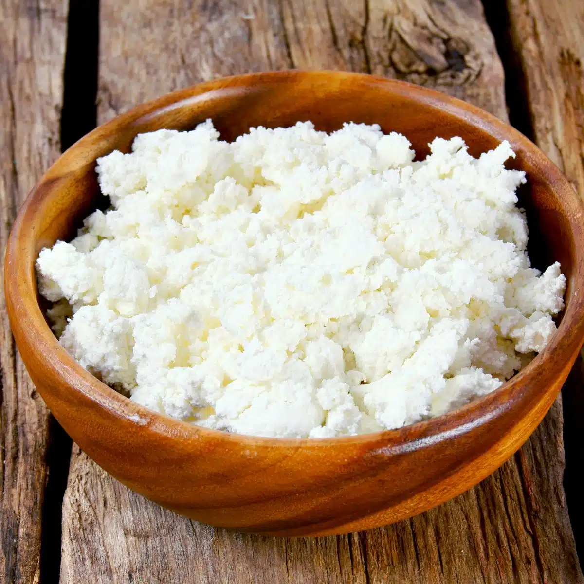 Square image of cottage cheese in a wooden bowl.