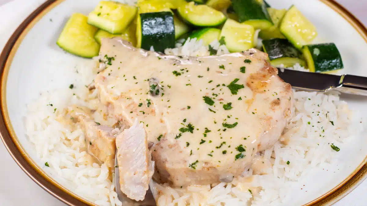 Wide image of cream of mushroom pork chops on a plate over rice with zucchini on the side.