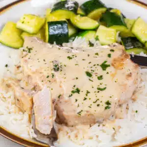 Square image of cream of mushroom pork chops on a plate over rice with zucchini on the side.