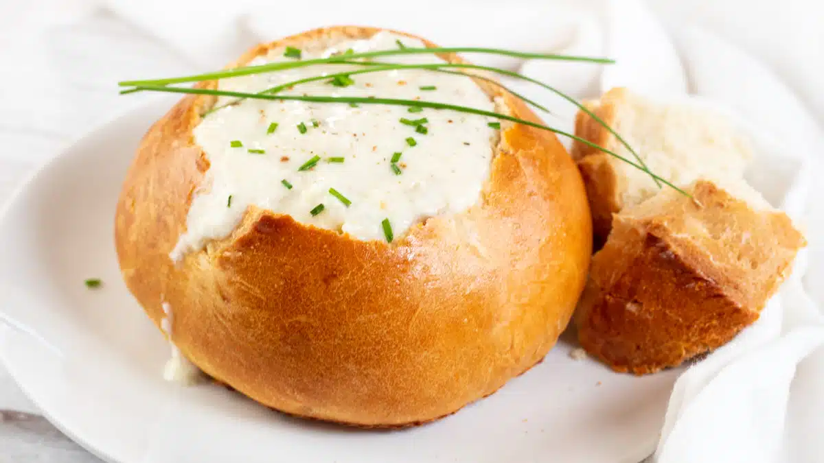 Wide image showing a homemade bread bowl filled with soup.
