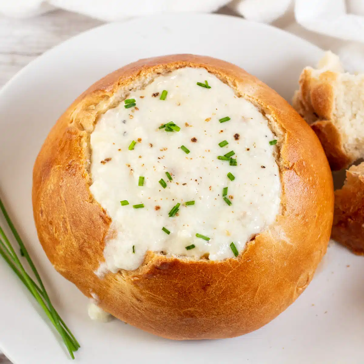 Square image showing a homemade bread bowl filled with soup.