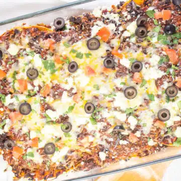 Wide image of Mexican lasagna in a glass baking dish.