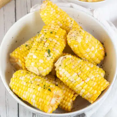 Square image of a white bowl full of steamed corn on the cob.