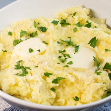 Wide image showing cream cheese mashed potatoes in a white bowl with butter and chives.