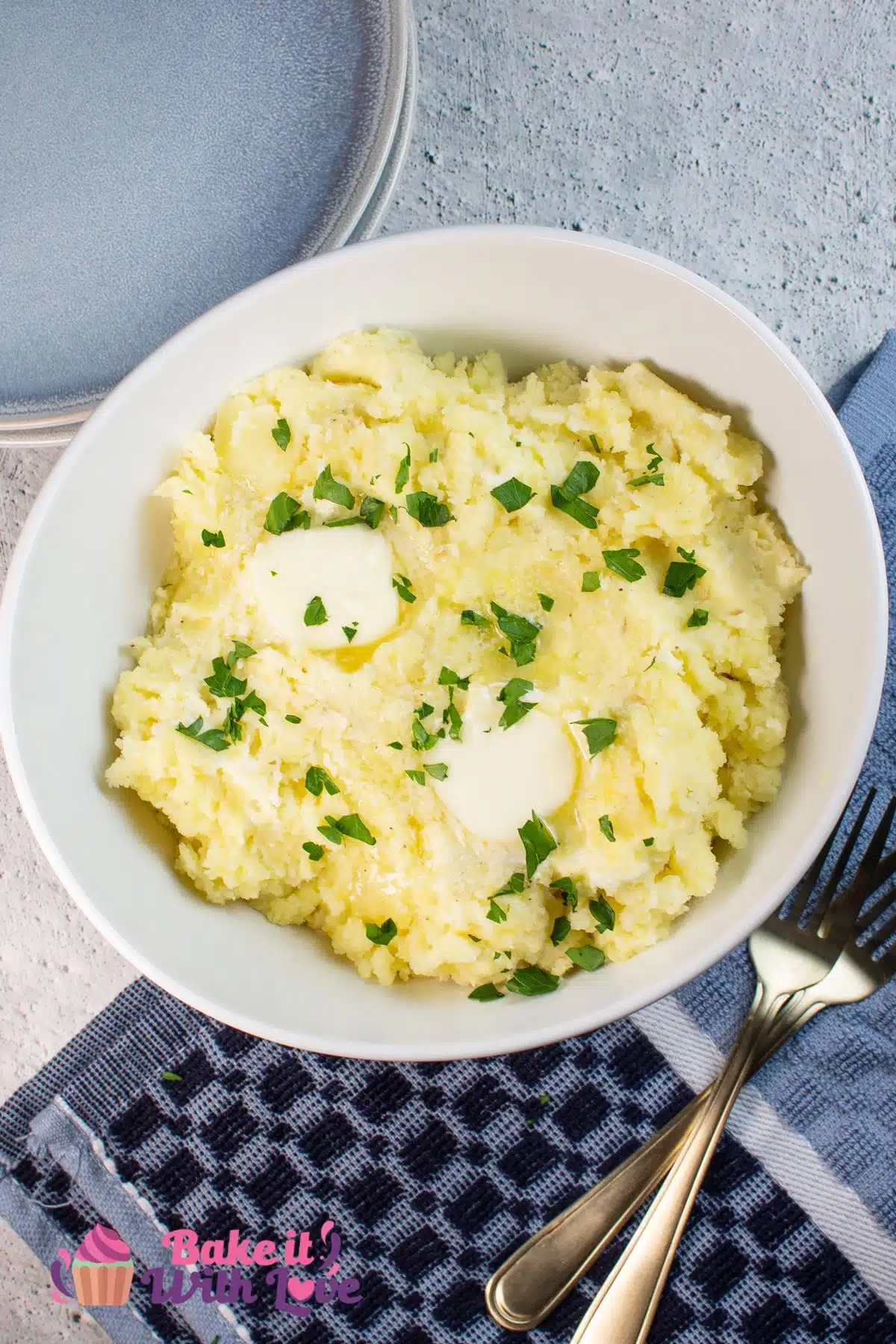 Tall image showing cream cheese mashed potatoes in a white bowl with butter and chives.