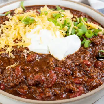 Wide image of Dutch oven chili in a bowl with grated cheddar cheese and sour cream on top.