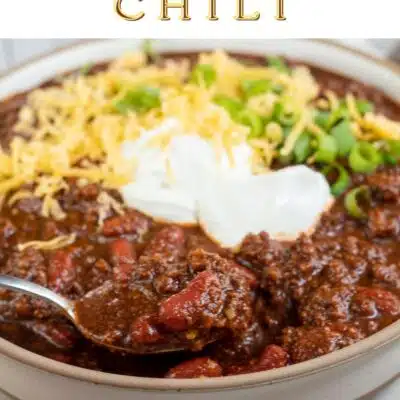Pin image with text of Dutch oven chili in a bowl with grated cheddar cheese and sour cream on top.