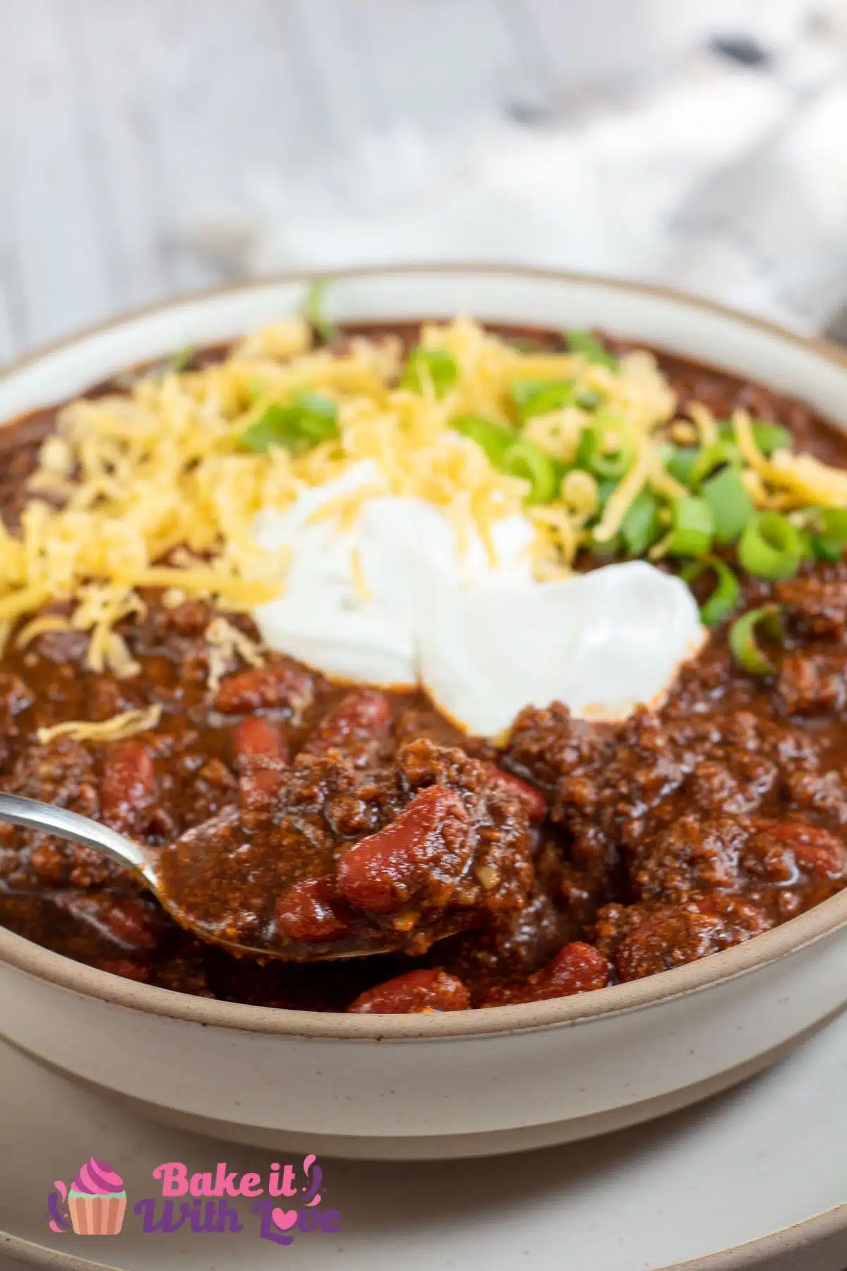 Tall image of Dutch oven chili in a bowl with grated cheddar cheese and sour cream on top.