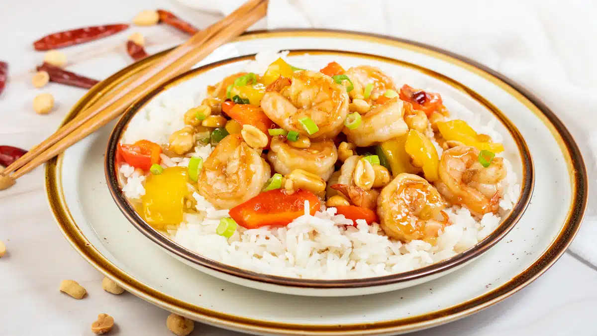Wide image of kung pao shrimp on a plate with white rice.