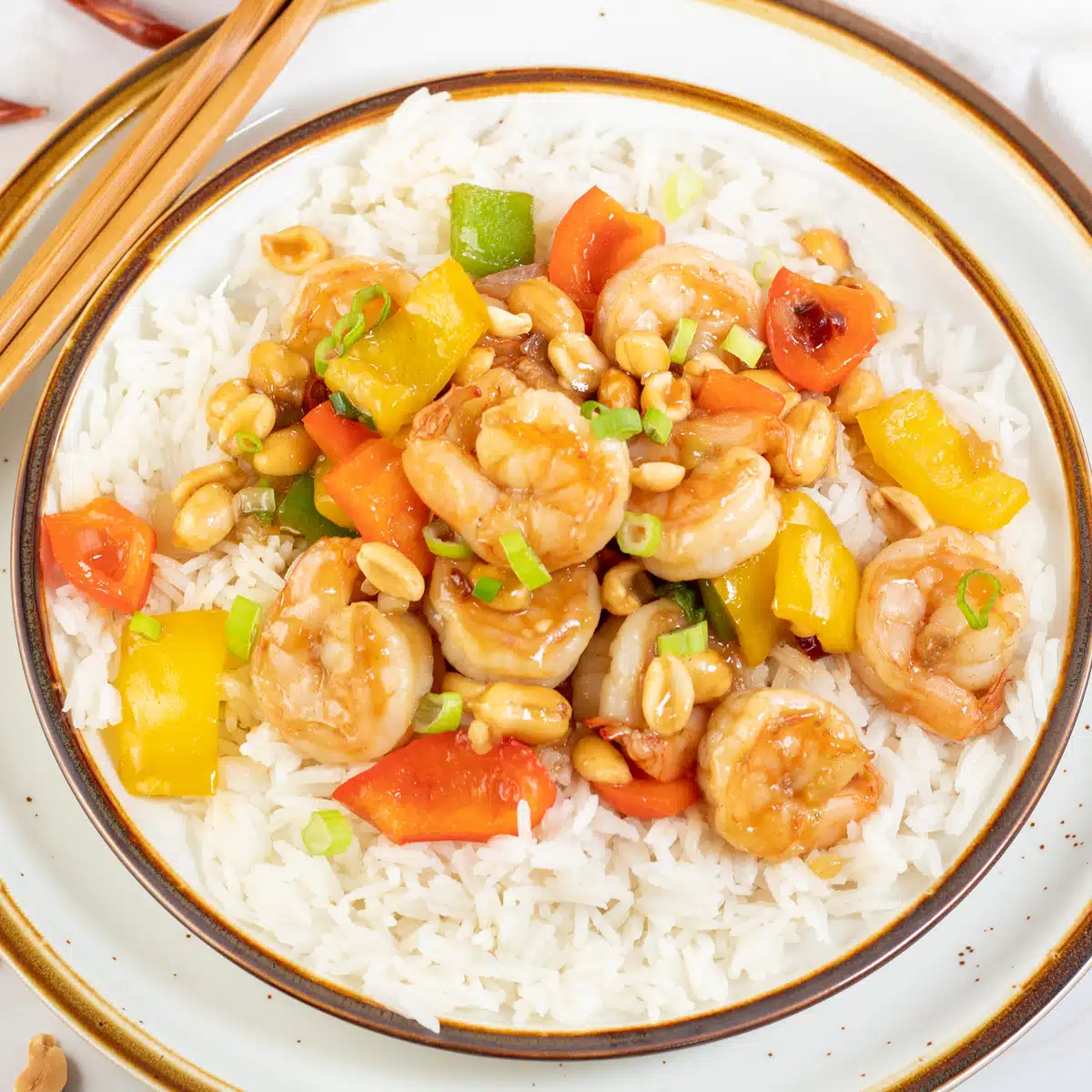 Square image of kung pao shrimp on a plate with white rice.