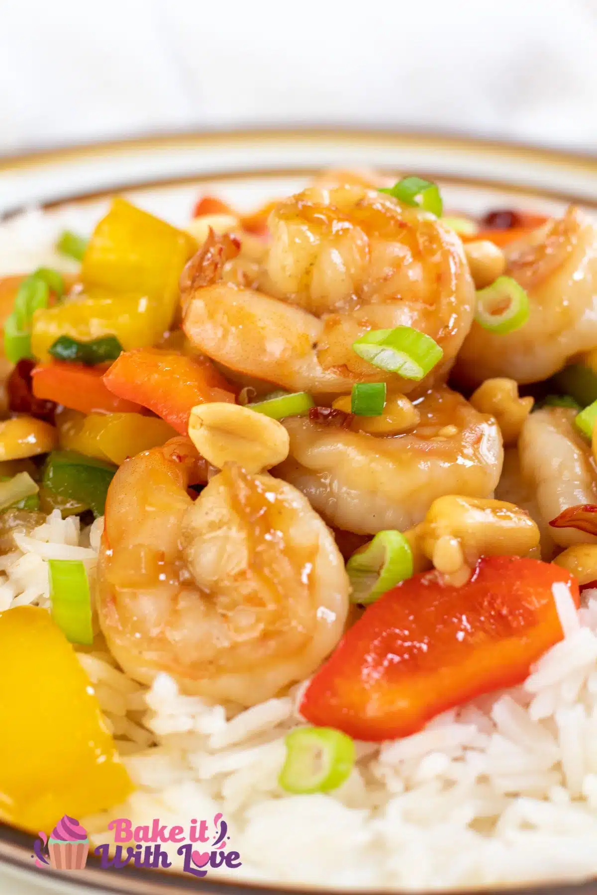 Tall close up image of kung pao shrimp on a plate with white rice.
