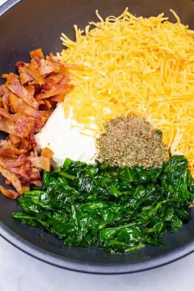 Process image 3 showing mixing bowl with cream cheese, chopped bacon, sauteed spinach, cheese, and seasoning.