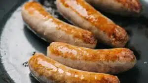 Wide image of Italian sausages in frying pan.