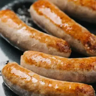 Square image of Italian sausages in frying pan.