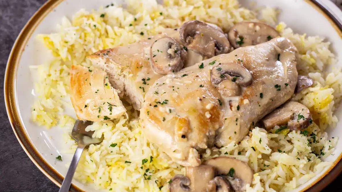 Wide image of mushroom chicken over rice on a plate.