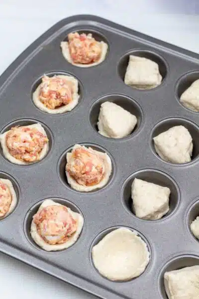 Process image 5 showing sausage filling added to biscuits dough in mini muffin tin.
